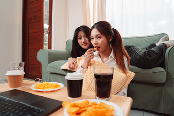 Asian Women Snack Food Eating Lifestyle Indoor Living Room Enjoyment Movie, Two Young Adults Sharing Laughter and Snacks While Watching TV, Embracing Friendship and Relaxation at Home Together