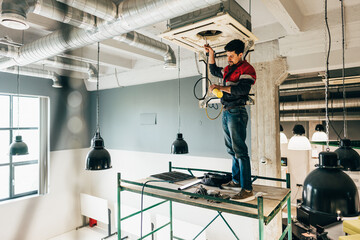 Worker installs ventilation system in modern commercial space during daylight hours