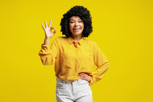 Young woman showing ok sign with positive facial expression on yellow background