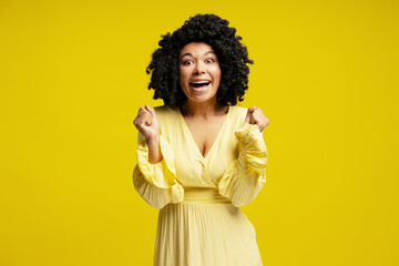 Enthusiastic woman celebrating with raised fists on yellow background