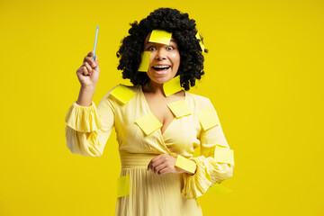 Enthusiastic businesswoman having an idea while covered in sticky notes on yellow background