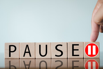Hand pointing to a wooden block with a pause symbol, next to blocks spelling 'PAUSE'. Concept of...