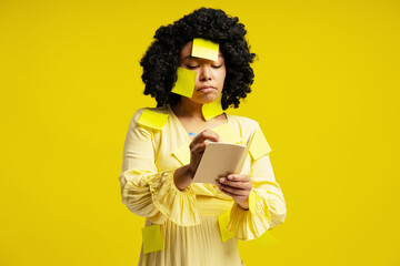 Businesswoman writing notes on notepad covered with yellow sticky notes