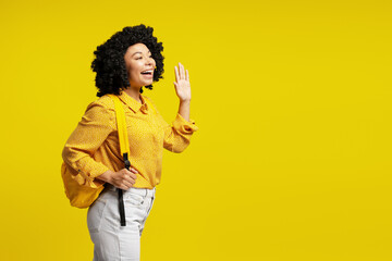 Young student shouting and greeting someone on yellow background