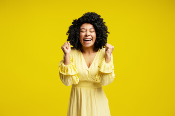 Enthusiastic african american woman celebrating success on yellow background