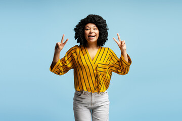 Cheerful young woman showing peace sign with both hands and smiling on blue background