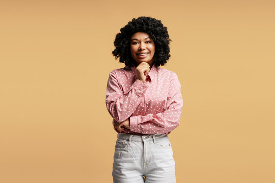Young woman touching chin, smiling and thinking, isolated on beige background - Powered by Adobe