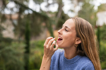 Young woman taking vitamin pill outdoors, promoting health and wellness