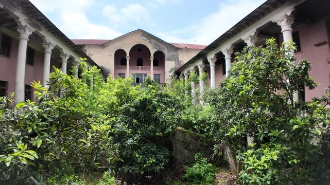 Lush vegetation reclaiming the courtyard of the abandoned Sanatorium Gelati in Georgia, with decaying columns and a crumbling facade evoking a forgotten luxury past