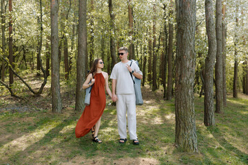 Fototapeta premium Couple walking hand in hand through a sunny forest during springtime