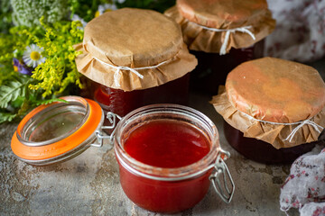 Home cooking: plum jam in a glass jar on a gray background. Close-up