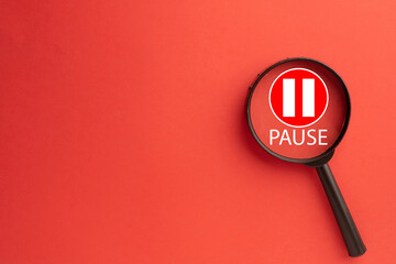Magnifying glass focusing on a red pause button icon with white bars and 'PAUSE' text.Concept of taking a break,stopping for reflection, work hiatus,analyzing an interruption,or media player control.