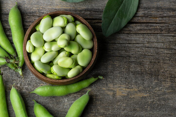 Fresh broad beans with pod in bowl on wooden background, healthy food