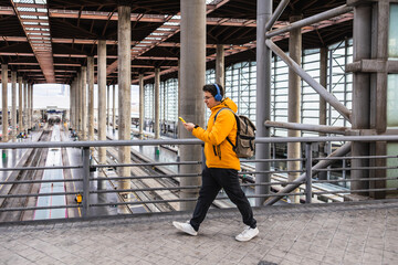 Traveler walking in train station using smartphone and headphones