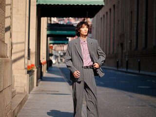 Portrait of handsome Chinese young man wearing gray suit posing in the street, young guy with black curly hair with urban background. Male fashion, cool Asian young man lifestyle.