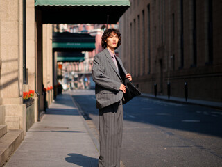 Portrait of handsome Chinese young man wearing gray suit posing in the street, young guy with black curly hair with urban background. Male fashion, cool Asian young man lifestyle.