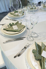 Formal dining table with elegantly arranged glassware, plates, and green napkins. Central floral arrangement features white roses and candles, creating a refined atmosphere.