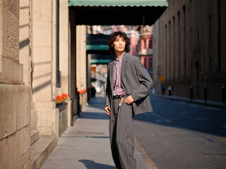 Portrait of handsome Chinese young man wearing gray suit posing in the street, young guy with black curly hair with urban background. Male fashion, cool Asian young man lifestyle.