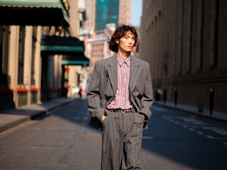 Portrait of handsome Chinese young man wearing gray suit posing in the street, young guy with black curly hair with urban background. Male fashion, cool Asian young man lifestyle.