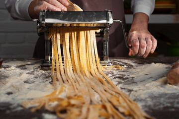 Caucasian female hands making fettuccine noodles using mechanical pasta machine