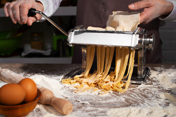 Caucasian female hands making fettuccine noodles using mechanical pasta machine