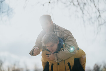 A cheerful outdoor scene of two friends bonding and having fun on a sunny winter day. One is giving...