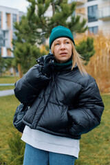 Portrait of a young woman in a jacket and hat who is talking on the phone against the background of a residential area