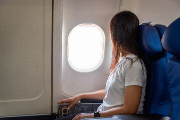 Girl plane passenger sits in an airplane and looking at the view at the plane window.