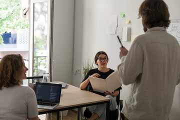Three software developers brainstorming in a modern office. Team coding session with laptops...