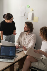 Three software developers brainstorming in a modern office. Team coding session with laptops...