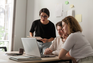 Three software developers brainstorming in a modern office. Team coding session with laptops...