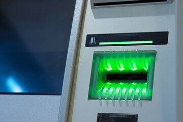 A closeup of a glowing green card slot of an ATM, ready to accept a transaction card.