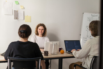 Three software developers brainstorming in a modern office. Team coding session with laptops...