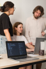 Three software developers brainstorming in a modern office. Team coding session with laptops showing code, planning web development and design. Tech startup environment and teamwork