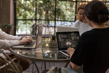 Three software developers brainstorming in a modern office. Team coding session with laptops...