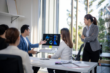 A group of people are in a meeting room with a computer monitor showing graphs