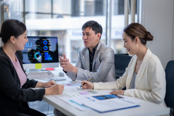 Three people are sitting at a table with a computer monitor in front of them