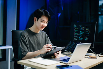 Young male programmer working with tablet and screen displaying code. Modern tech office setup, great for software, coding, IT..