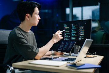 Young male programmer working with tablet and screen displaying code. Modern tech office setup, great for software, coding, IT..