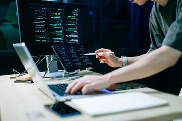 Programmer using stylus and laptop to write code at night. Coding workspace with tablet, monitor, and dark theme
