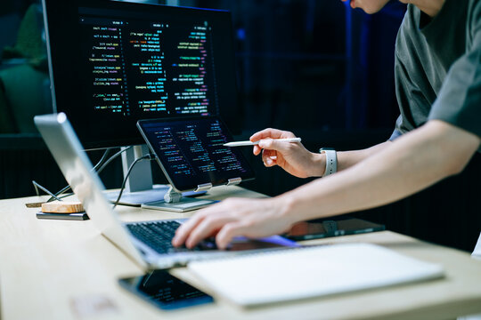 Programmer using stylus and laptop to write code at night. Coding workspace with tablet, monitor, and dark theme