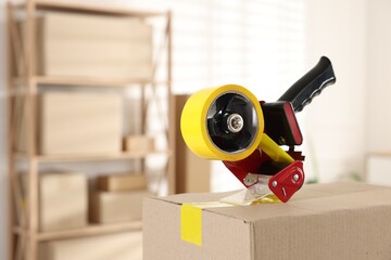 Dispenser with adhesive tape on cardboard box indoors, closeup