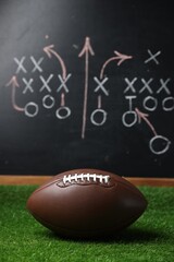 American football ball on green grass against chalkboard with game scheme