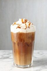 Tasty iced coffee with whipped cream and syrup on white marble table