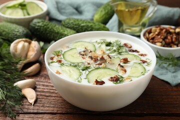 Tasty cucumber soup with dill and nuts in bowl on wooden table, closeup