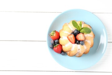 Tasty Bundt cake with powdered sugar and berries on white wooden table, top view. Space for text