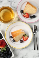 Pieces of tasty bundt cake with berries and tea on white marble table, flat lay