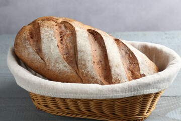 Loaf of bread in basket on grey wooden table, closeup