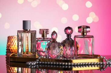 Many different perfume bottles and accessories on mirror surface against pink background with...