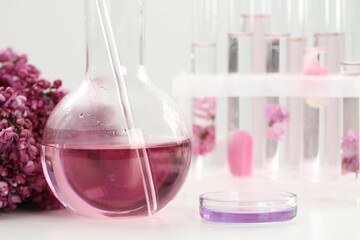 Making luxury perfume. Essential oils in glassware and flowers on white table, closeup